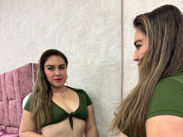 TaylorNova, avec de longs cheveux bruns, un haut vert noué sous sa poitrine, du rouge à lèvres, regardant son reflet, portant une chemise verte, dans une pièce avec un fauteuil rose rembourré..