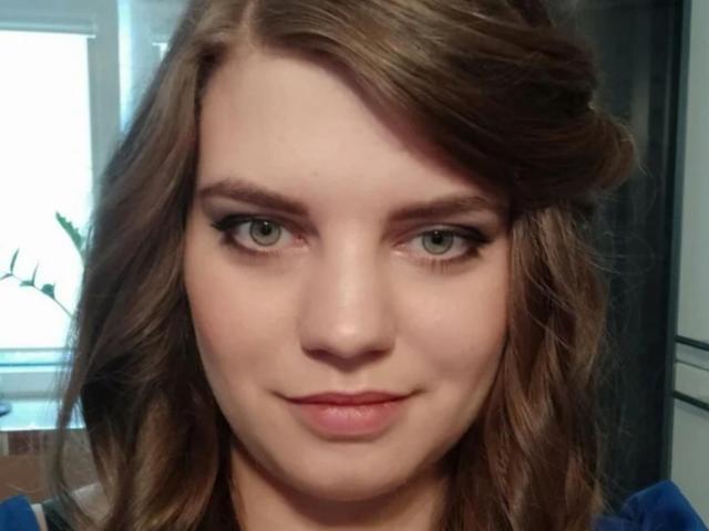 AdrianaGlow tiene el pelo castaño ondulado, ojos verdes y una ligera sonrisa. Lleva una camisa azul, y no se ve su trasero. Su maquillaje es discreto y es atractiva..