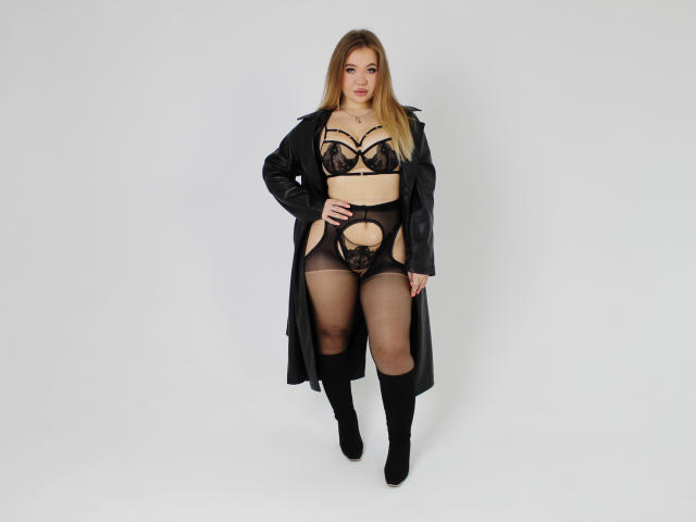 StacyYellig in black lingerie with cutouts, showing her big ass and small tits, wearing a long black coat and black knee socks, standing with a confident, sexy look.