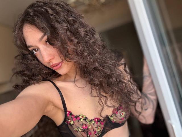 MoniFoxy's black leather shorts, hand gripping crotch, tattoo on right arm, visible thighs, slightly bent forward. Soft lighting, focus on lower body.