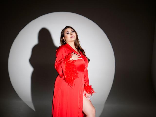 MysteriousLight with large tits, wearing a red satin robe with fluffy cuffs, standing against a white circular shadow, looking up with a slight smile, brown hair, fair skin.