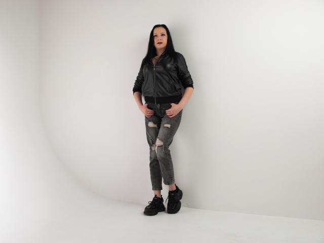 ElizabethSo stands with hands on ripped gray jeans, black leather jacket, and black sneakers, showing a cute ass, dark red lipstick, and long black hair.