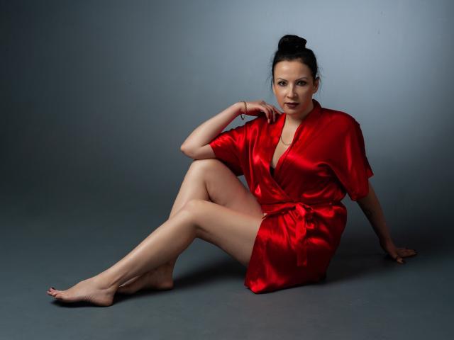 ElizabethSo sits on the floor wearing a shiny red silk robe, legs crossed, arms resting on her knee, looking at the camera with a slight smile, black hair in a bun.
