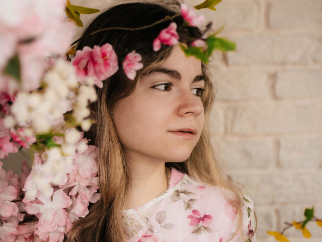 TinaRedly with pink and white flowers in her brown hair, wearing a floral pink dress, looking to the side with a soft expression, her ass slightly visible.