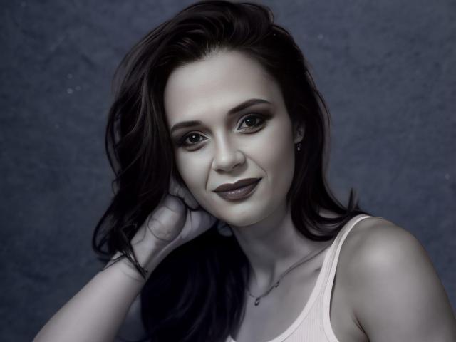 SweeteestJulie with dark, wavy hair, pale skin, and dark lipstick, smiling at the camera, hand touching her head, wearing a pink tank top, gray background.