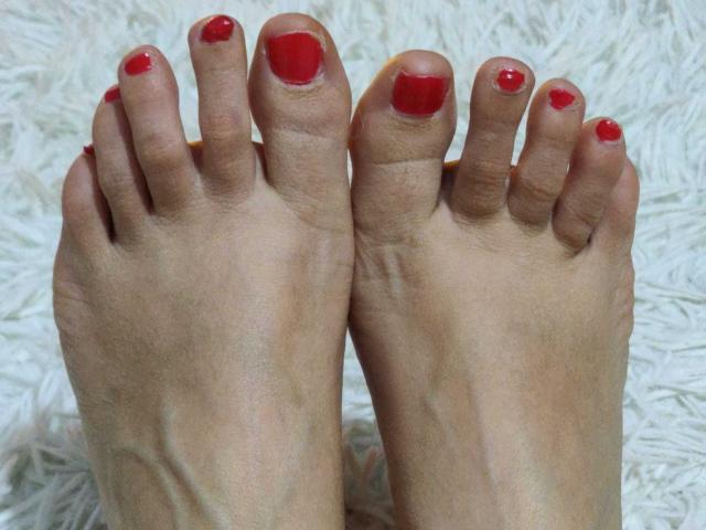 SweeteestJulie's feet, showing her toes with shiny red nail polish, positioned side by side, against a fluffy white surface. Her skin is light and slightly wrinkled.