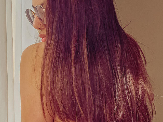NaturalMariaHun with long, straight brown hair covering her bare back, wearing round glasses, looking over her shoulder. Boobs slightly visible. Soft light. NaturalHun's face partially in frame.