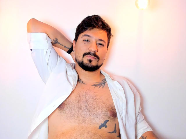 DavidEvans, a hairy-chested guy with tattoos, white shirt open, arm behind head, looking at camera, slight beard, mustache, brown hair, light skin, confident, relaxed, upper body.