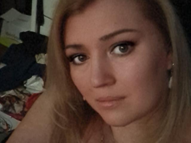 CamilleJazz has blonde hair, blue eyes, and a slightly serious expression. She's wearing small earrings and looking directly at the camera with subtle makeup.
