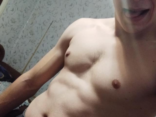 FortuneNorman's bare, muscular chest with small, pink nipples. His skin is light, and his mouth is slightly open. A small, greenish tooth is visible.