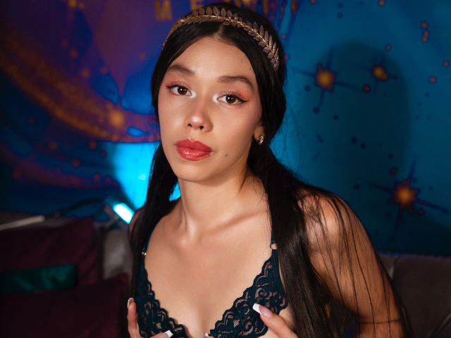 Rose, con lunghi capelli neri, indossa un reggiseno nero in pizzo, tiene le sue piccole tette, ha il rossetto rosso e una fascia dorata, su uno sfondo blu con un motivo a stelle..