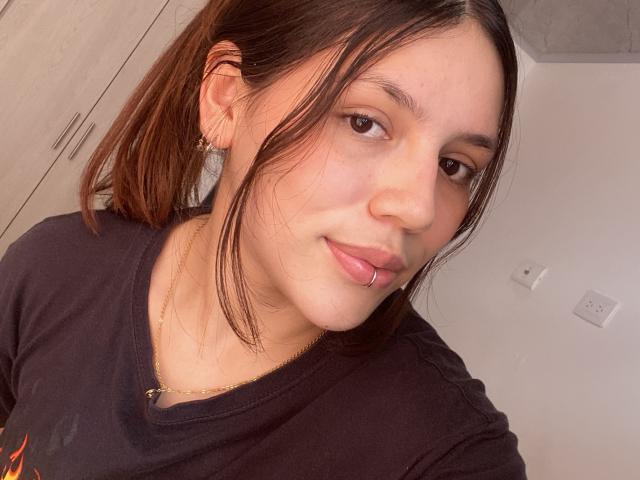 SophiaMarx has a cute face with brown eyes, a small nose, and a lip ring. She's wearing a black shirt, has a gold necklace, and brown ponytail.