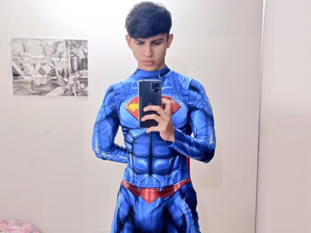 WillStarr, wearing a blue Superman costume with a red belt and yellow 'S' logo, taking a mirror selfie with a serious expression, holding a black phone.