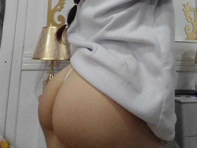 MadisonAngel's ass in a white shirt, showing a pale, smooth butt in a thin, white thong. Her shirt is slightly raised, exposing her butt.