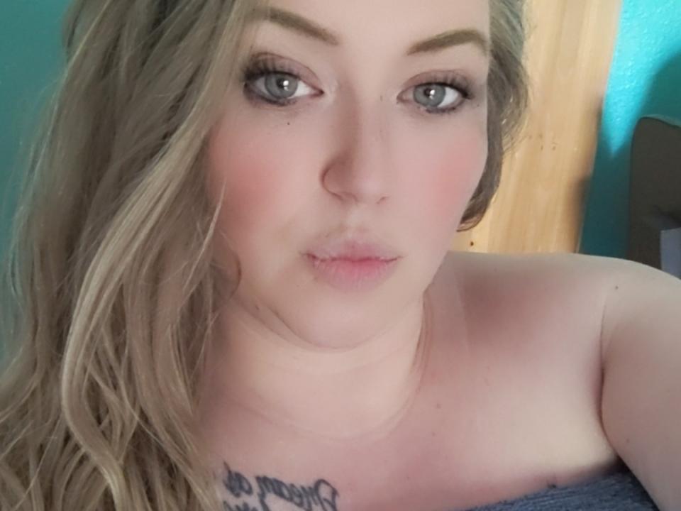 SeductiveBlondie69 with pale skin, blue eyes, and blonde hair, pouty lips, subtle makeup, and a tattoo below her tits, wrapped in a blue towel, looking directly at the camera.
