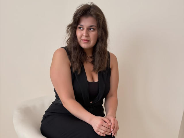 SublimeMature with wet brown hair, purple lipstick, and red lace top showing tits and armpit, against a pink wall. Top has criss-cross straps and lace pattern.