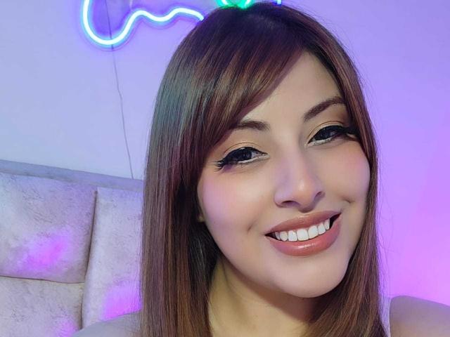 AlexaQueenOne with long brown hair, smiling with full lips and white teeth, neon cat headlight above her head, wearing black eyeliner and pinkish nude lipstick.