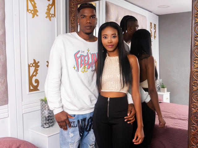 CataleyaAndEthan, a dark-skinned man with a muscular build, wears a white "Freedom" sweatshirt and ripped jeans. Next to him, a dark-skinned woman with long black hair wears a white crop top and black pants.