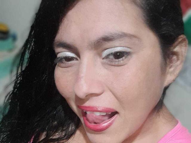 Luciana Montiel, avec ses cheveux noirs mouillés, sa langue tirée et portant un soutien-gorge rouge, exhibe sa peau bronzée et ses petites seins. Son expression est espiègle et légèrement ridicule..