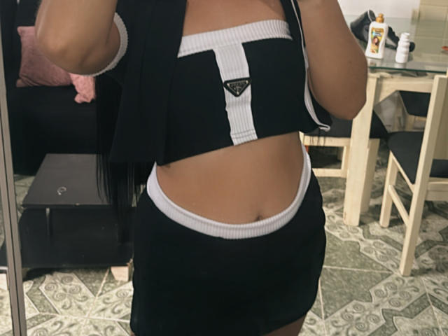 SarahGood's midriff shows black and white sports bra with white stripe, black skirt with white trim, and black jacket, exposing her flat stomach and slightly visible belly button.