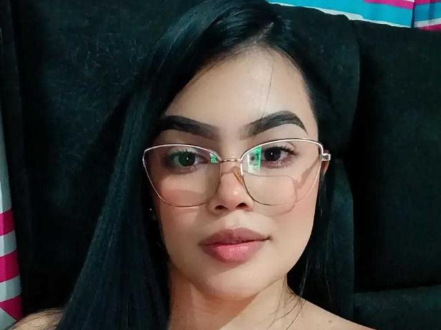 SammyOne with black hair, brown eyes, and glasses, has a cute face, full lips, and a slight smile. She's looking straight at the camera, with a neutral expression.