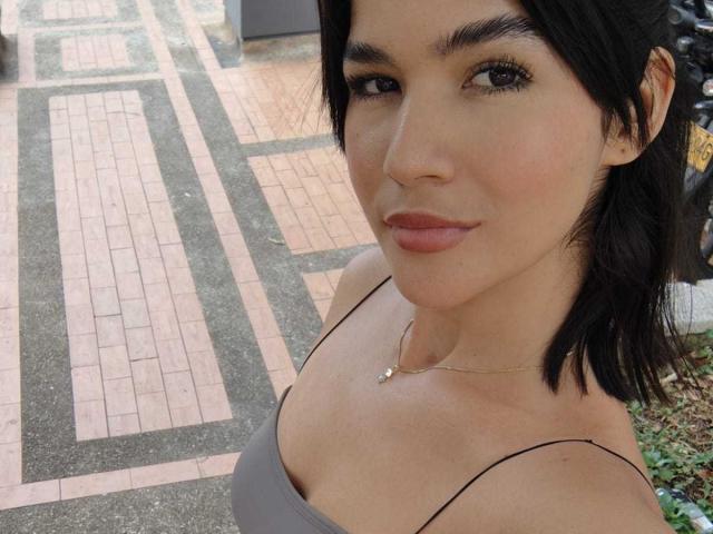 ScarlletZhen with dark hair, light brown skin, small gold necklace, gray off-shoulder top, subtle smile, and full lips. Boobs visible, brown eyes, black eyeliner.