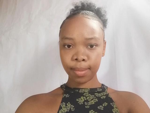 Leanah has dark brown skin, small nose, and curly black hair in a bun. She's wearing a black halter top with green floral patterns, showing her bare shoulders.