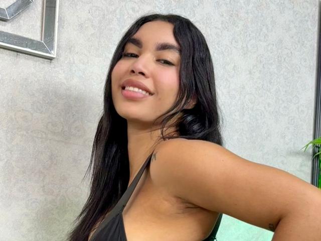 LaureneX has long black hair, tan skin, and is smiling with her tongue slightly out, wearing a black top that shows her side boob and armpit.