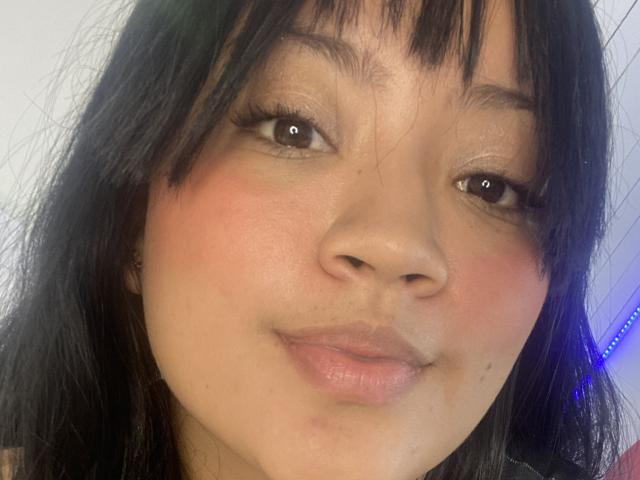 JulietaDuval's face with dark black hair, brown eyes, and pink blushed cheeks, slightly smiling with her pink lips and a small nose, looking directly at the camera.