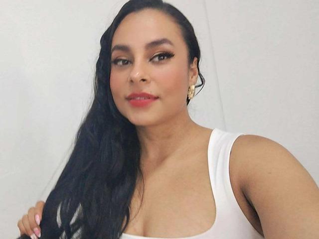 LunaSoler with long black hair, white tank top, and earrings, showing her tits, has a slight smile and red lipstick, holding her hair with one hand.