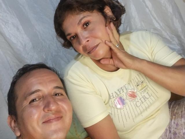 YazminaAndJason with short brown hair, yellow shirt, and hand on cheek, next to Jason with dark hair, smiling, wearing a ring. White background. Casual selfie.