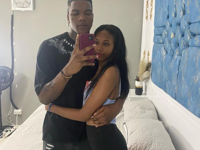 CataleyaAndEthan, femme noire en soutien-gorge bleu en dentelle, petits seins, debout, bras autour d'elle, CataleyaAndEthan, homme noir, torse nu, tenant un téléphone, lit en arrière-plan..