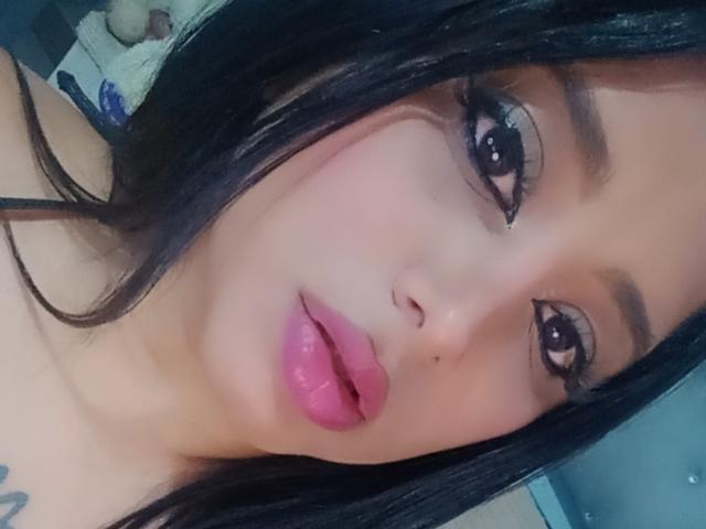 MariaCatalina's face, dark hair, pink lips, thick eyebrows, long eyelashes, and manicured fingers with pink nail polish. Her hand touches her cheek. Soft, youthful, attractive.