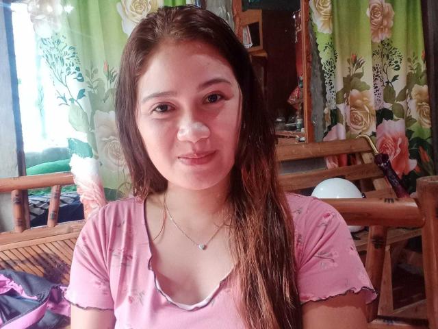 JailyHot with wet brown hair, pink floral shirt, small tits, light skin, subtle nose, small smile, necklace, wooden chair, floral curtains, mirror in background.