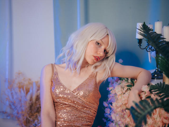 BrendaLovex with pale skin and platinum blonde hair, wearing a shimmering pink dress, has small tits and a cute face, leaning on a floral arrangement, looking sexy.