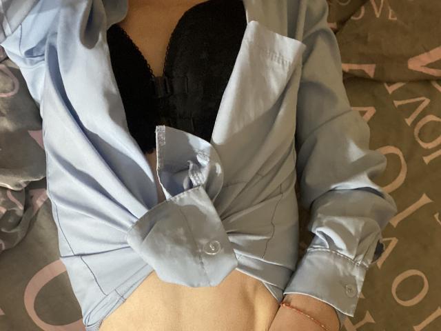 Kabblasha draagt een lichtblauwe blouse met opgestroopte knopen, waardoor haar zwarte, met kant bedekte borsten zichtbaar zijn, en ze heeft een rode armband om haar rechterpols. Ze ligt op een bed..