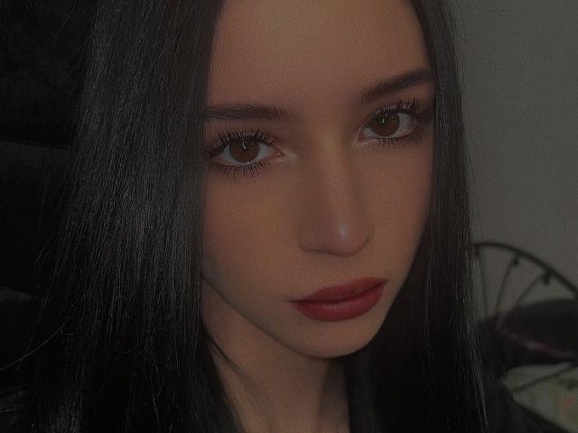 AnayaSweety's face with long black hair, brown eyes, and red lipstick. Her skin is smooth and she's looking slightly to the side with a serious expression.