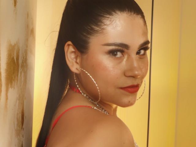 Pamela Owen tiene un rostro atractivo, de piel bronceada, con cabello oscuro y peinado hacia atrás, lápiz labial rojo y grandes aros de plata. Lleva una correa roja y está mirando por encima del hombro..