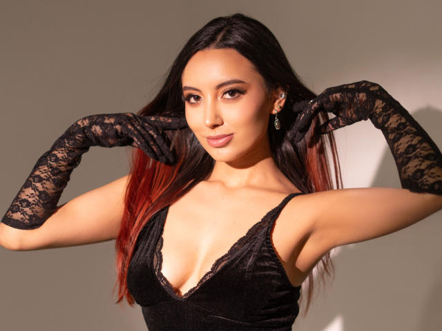 CarlaFranco, con lunghi capelli scuri, con le punte rosse, indossa guanti di pizzo nero e un abito nero scollato, che mette in mostra il suo seno e sorride con sicurezza..