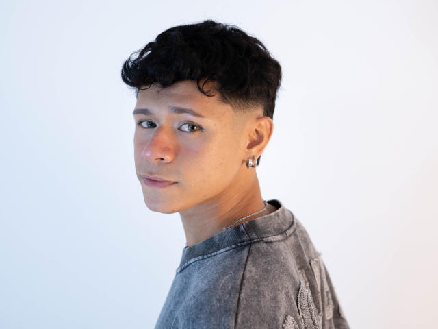 DanteEvans has short curly black hair, brown eyes, and a subtle smile. He's wearing a gray, slightly worn-out shirt with small holes. He's looking over his shoulder.