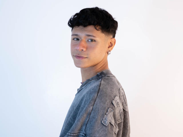 DanteEvans has short curly black hair, a silver earring in his left ear, and is wearing a gray, slightly worn-out, denim shirt. His face is turned slightly to the right.