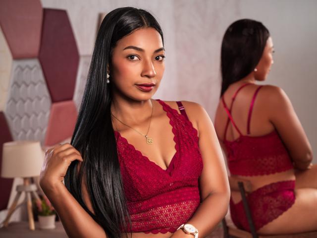 EmmaColeman69 with long black hair, wearing red lace lingerie, showing her small tits and ass in a mirror, looking at the camera with a slight smile.