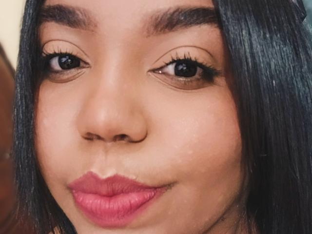SarahSmity's face with dark straight hair, brown eyes, and pink lipstick, showing a slight pout. Her eyebrows are thick and she has long eyelashes.