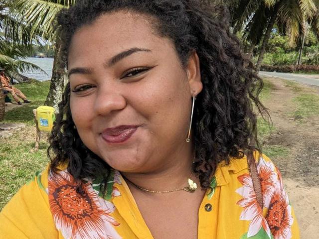 WendyStar69 has curly black hair, brown eyes, and is wearing a yellow floral shirt. She's smiling with pouty pink lips, showing a small tattoo near her chin.