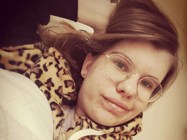 Tessa35-hot usa óculos, tem cabelo castanho claro e um moletom com estampa de leopardo, está deitada na cama com um rosto sonolento, levemente inchado e uma pequena perfuração no nariz..