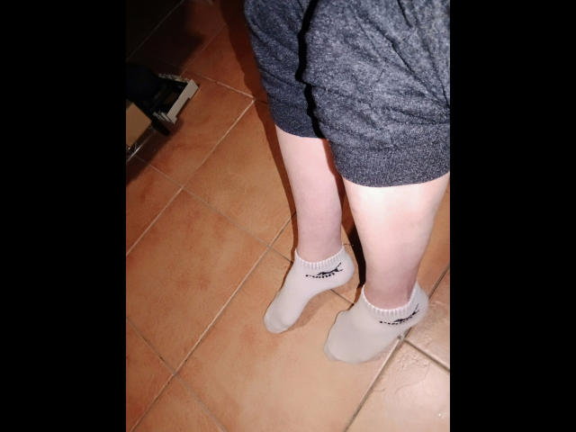 Madamecatsyve-hot's pale legs in beige ankle socks with black stripes, wearing dark gray shorts, standing on orange tile floor. Her socks and shorts are the only visible parts.