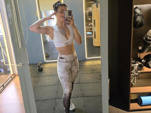 PaulinaValley with toned ass and small tits in a white sports bra and gradient-patterned leggings, taking a mirror selfie in a gym, showing off her fit, muscular body.