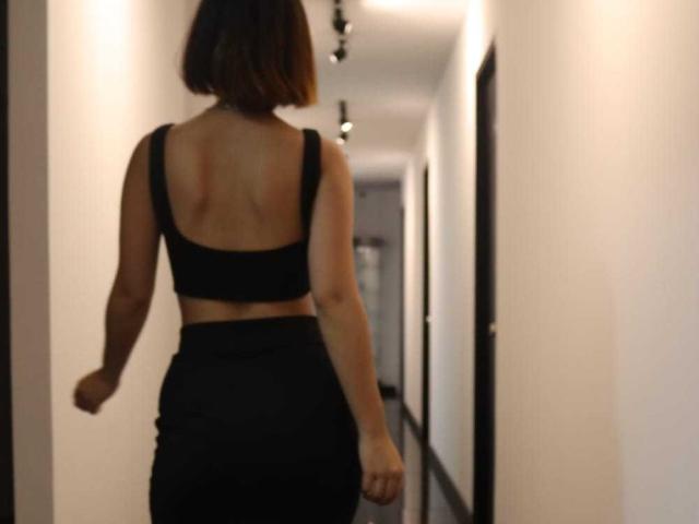 ViolettSoul heeft een achterwerk, draagt een zwarte crop top en een hoge taille rok, staat in een gang met haar rug naar de camera toe, en heeft een kort, bruin kapsel..