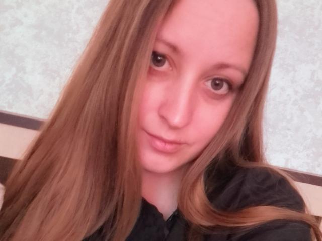 MonicaXRose has long brown hair, pinkish skin, and brown eyes, wearing a black shirt, with a slight smile, looking directly at the camera.
