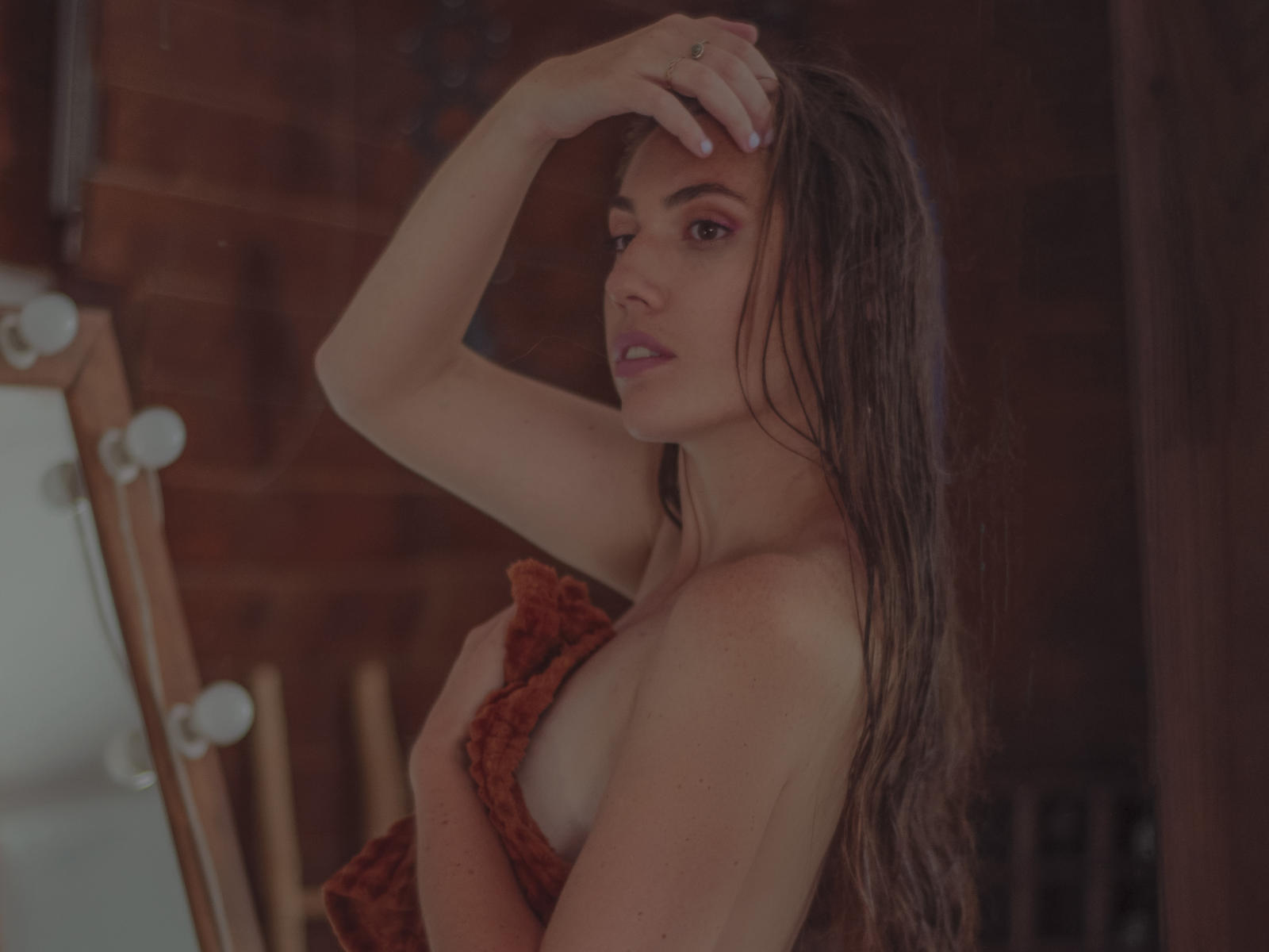 Sí, puedes hacerlo. Con el cabello castaño mojado, cubriendo sus pequeños senos con una prenda roja con volantes, con la mano en el cabello, mirando a la cámara, luz suave, fondo de madera..
